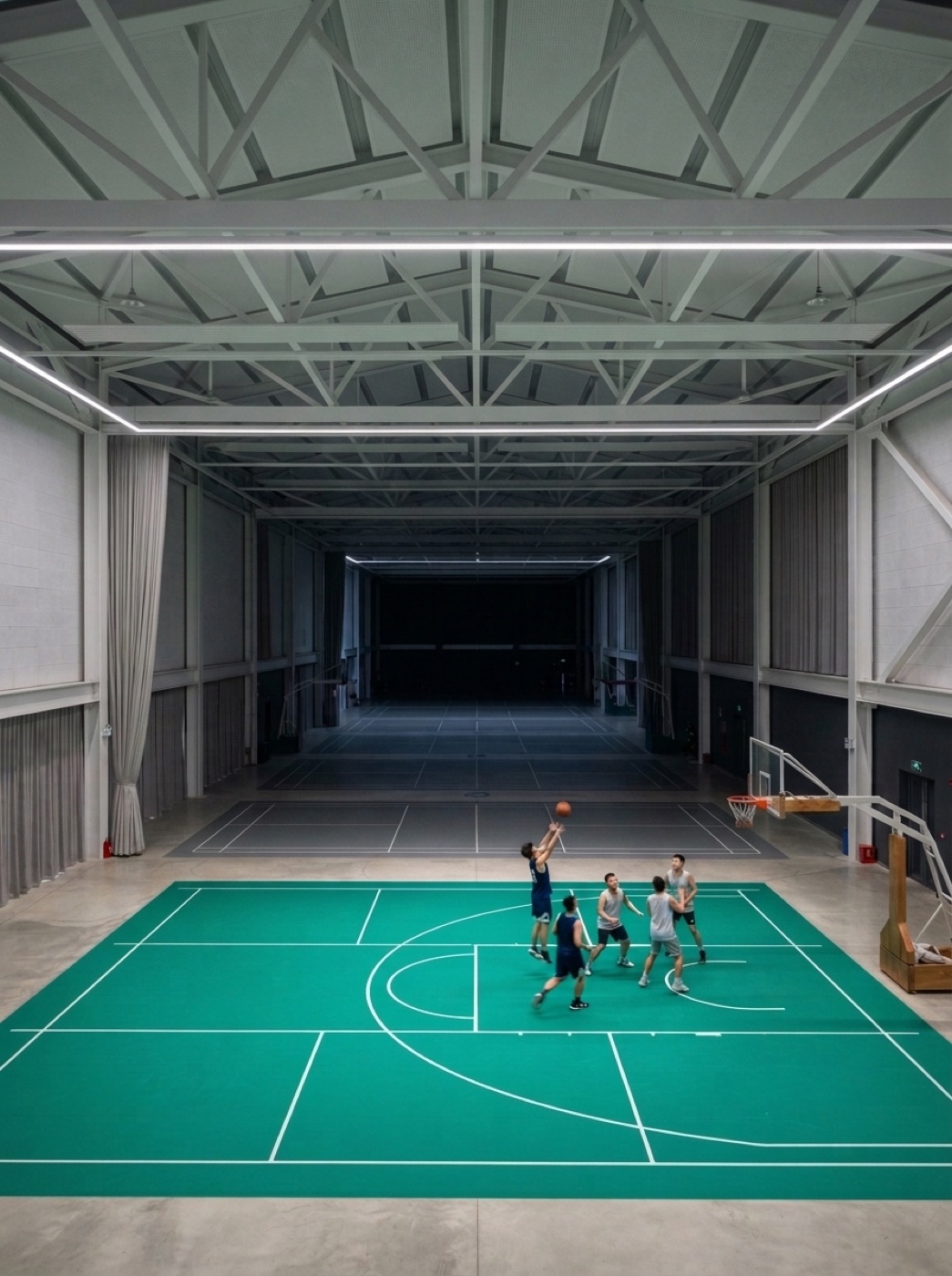 A large indoor sports hall, almost entirely empty, with a handful of players at one end.